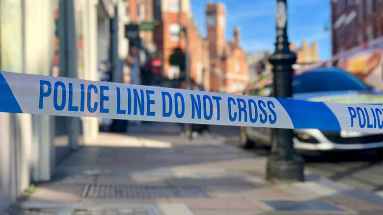 Image of generic uk highstreet pavement with police tape in front and police car visible behind