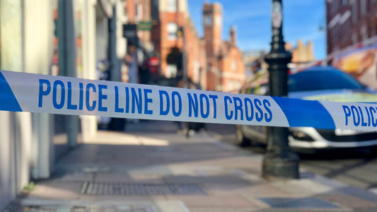 Image of generic uk highstreet pavement with police tape in front and police car visible behind