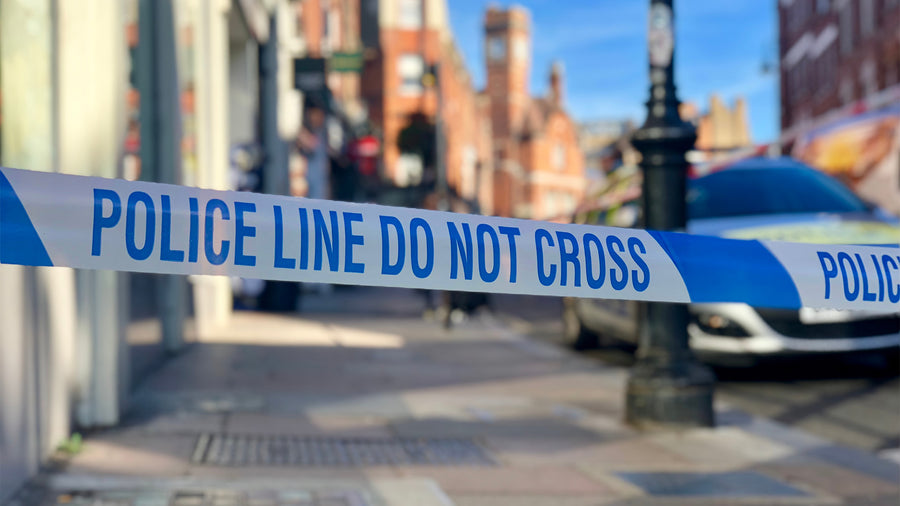 Image of generic uk highstreet pavement with police tape in front and police car visible behind